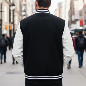 Person wearing a black and white varsity jacket walking down a city street. Showing from back