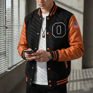 Person wearing a black and orange varsity jacket with an American flag patch, holding a phone.