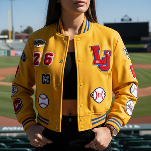 Person wearing a yellow varsity jacket with various patches on a baseball field.