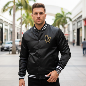 Man wearing a black varsity jacket with a logo on a city street