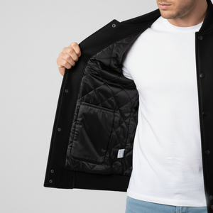 Person wearing a black jacket with quilted lining, white shirt, and blue jeans on a light gray background