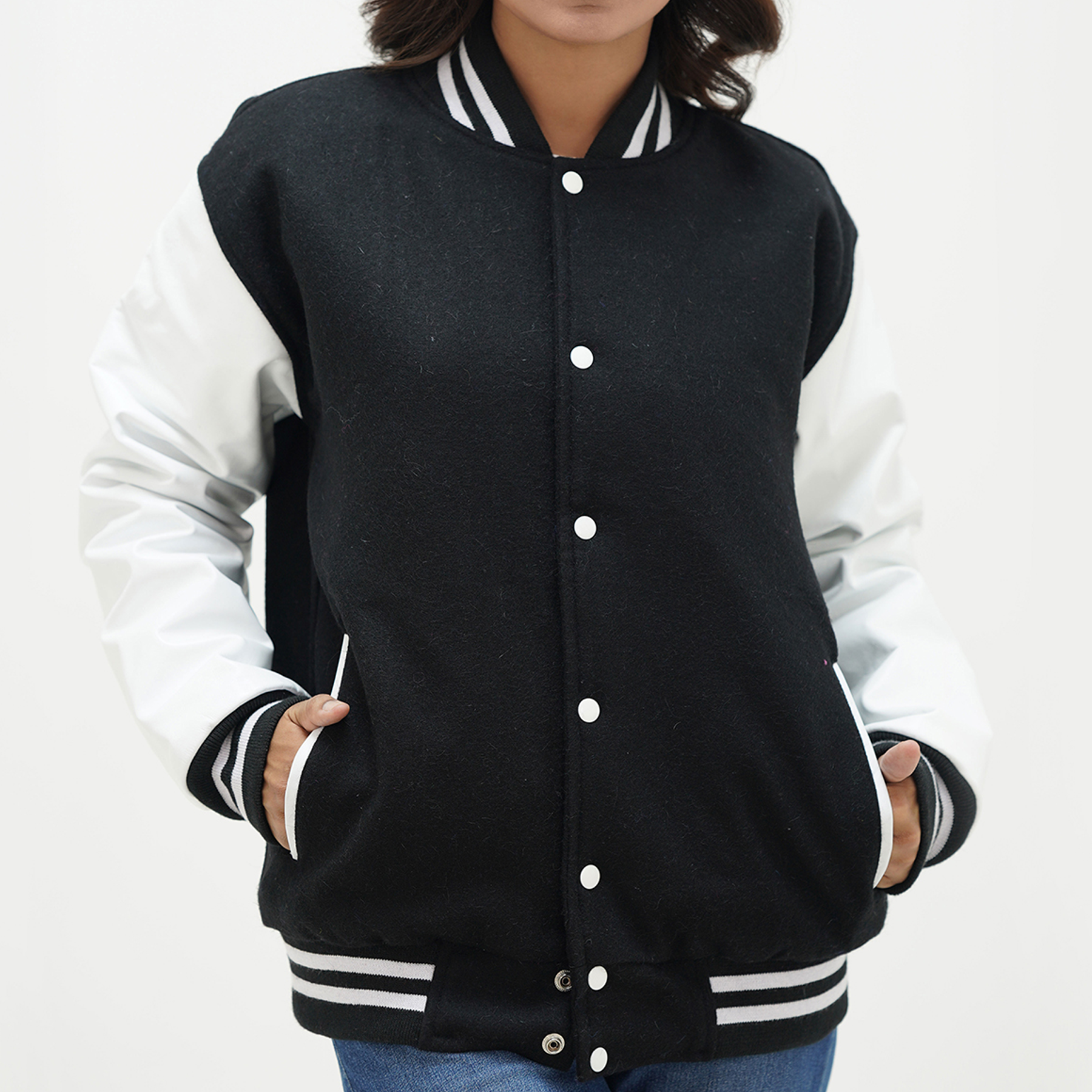 A woman wearing a black and white letterman jacket with leather sleeves, featuring a classic ribbed collar, ribbed cuffs, and a front with coated snaps. The jacket is displayed on a white background.
