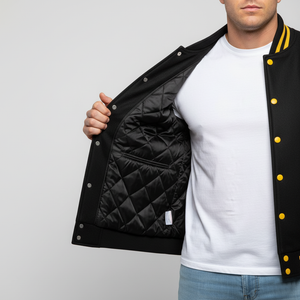 Person wearing a black varsity jacket with yellow buttons, open to reveal a quilted black lining.