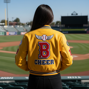Person wearing a yellow 'CHEER' jacket with a baseball design on a baseball field