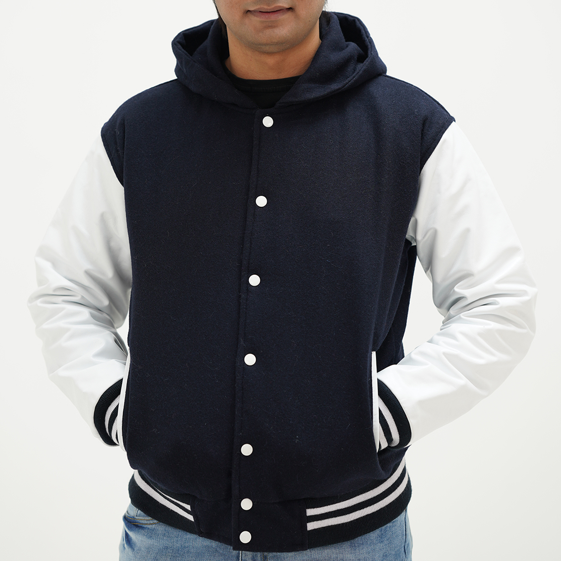 A man wearing a dark blue and white varsity jacket with a hood, featuring white stripes and a ribbed collar. The jacket has a front zipper and two side pockets.