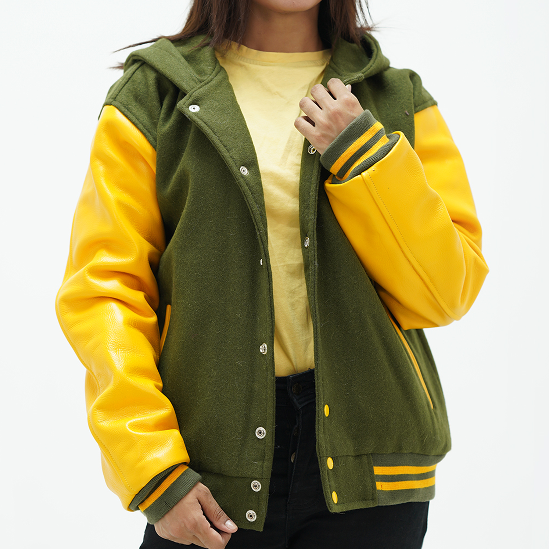 A woman wearing a green and yellow varsity hoodie with leather arms and a wool body, featuring a high collar, ribbed cuffs, and side pockets.