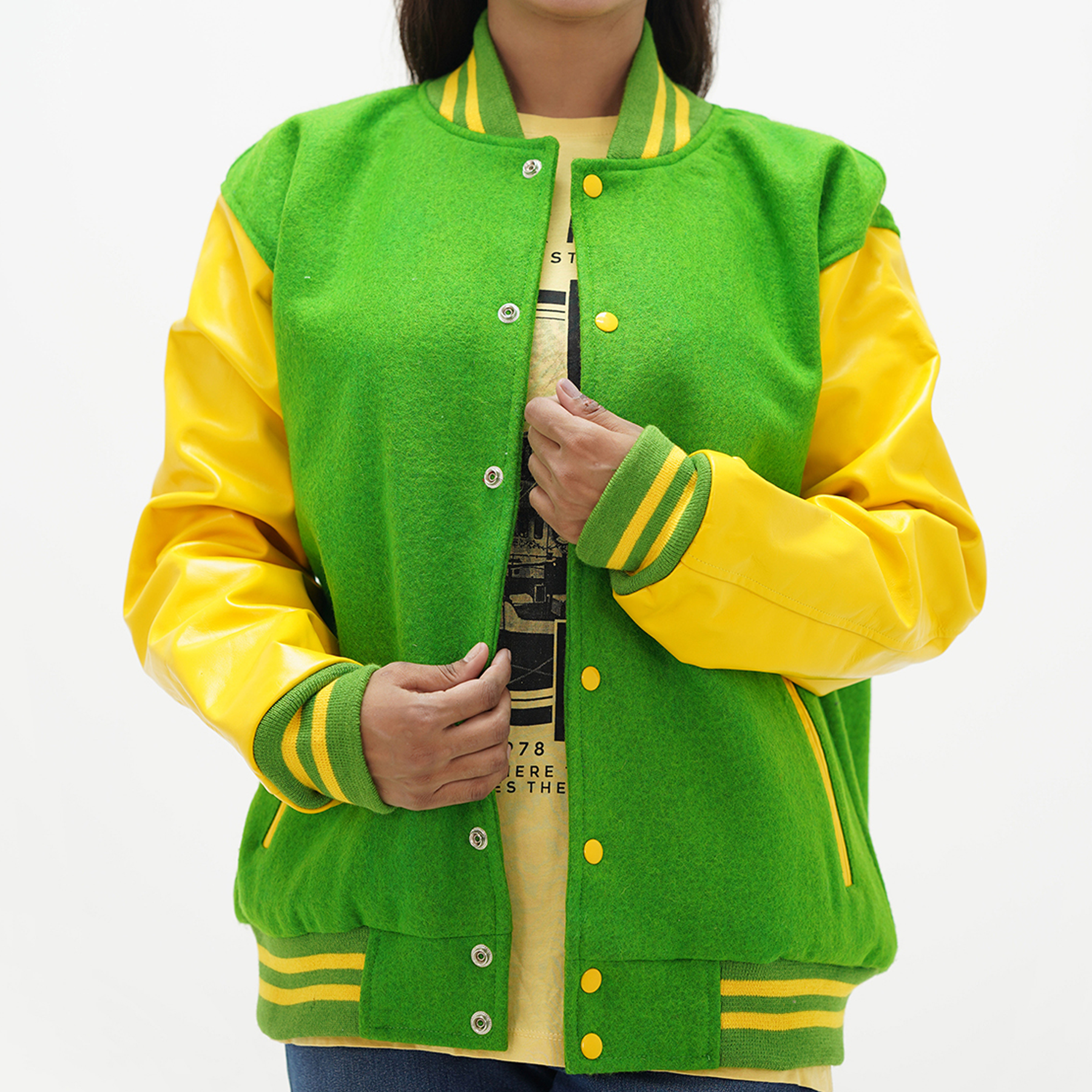 A woman wearing a Kelly green and yellow letterman jacket with leather arms and a wool body. The jacket features a quilted diamond lining, ribbed cuffs and hem, and is fastened with coated snaps.