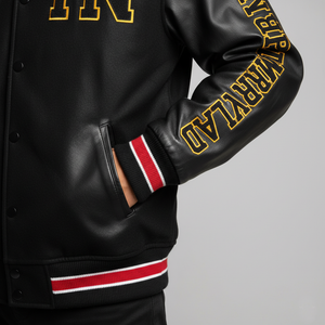 Black varsity jacket with yellow lettering on sleeves against a gray background