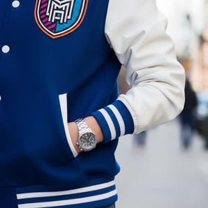Person wearing a blue and white varsity jacket with a watch on a blurred background