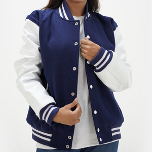 A woman wearing a navy blue and white letterman jacket with leather arms and a wool body. The jacket features a standing collar, front snaps, and side pockets.