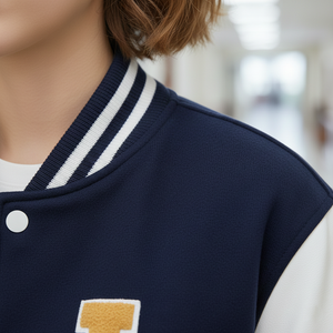 Navy blue varsity jacket with white trim and a logo on a blurred indoor background