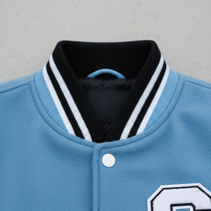 Close-up of a light blue varsity jacket with a black and white striped collar on a gray background.