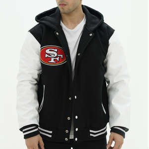 A man wearing a black and white San Francisco 49ers varsity jacket with leather sleeves and a hoodie. The jacket features a front snap closure and a stand-up collar.