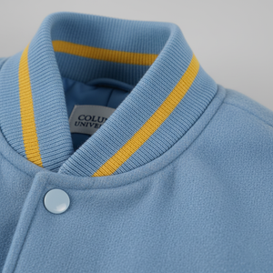 Close-up of a blue sweater with yellow trim and a button, featuring Columbia University branding.