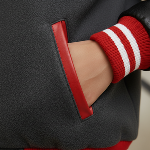 Close-up of a dark gray jacket with red trim and a red sleeve with white stripes.