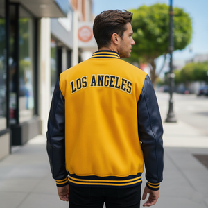 Man wearing a yellow and black 'Los Angeles' letterman jacket on a city street.