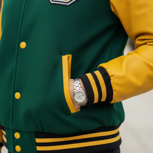 Green and yellow varsity jacket with a watch on a neutral background