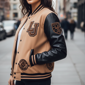 Person wearing a tan and black varsity jacket with logos on a city street.