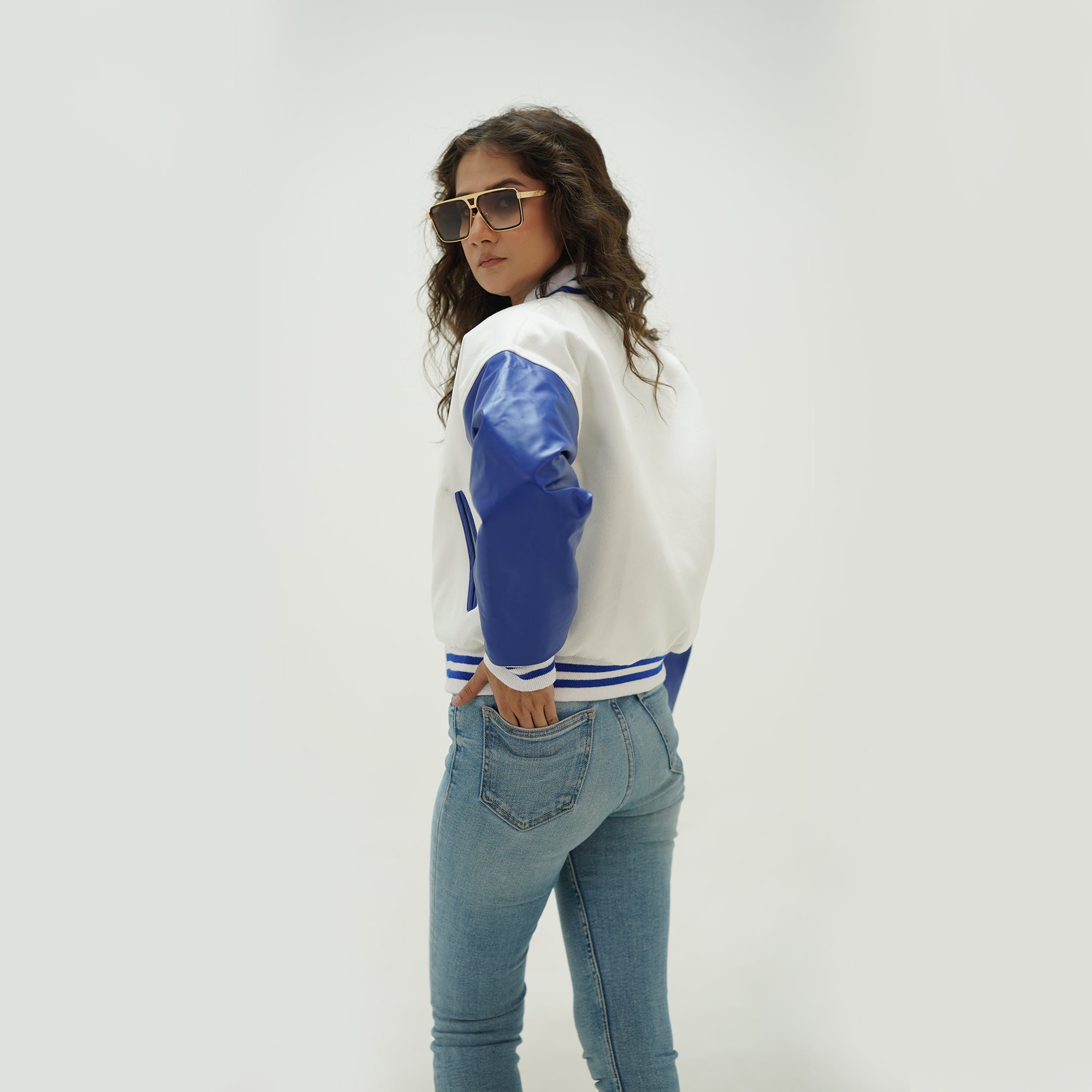 Back view of white and blue crop varsity jacket for women displaying white Melton wool body, blue genuine leather sleeves, and cropped ribbed hem