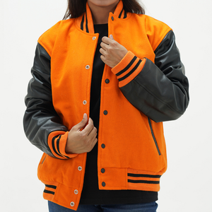 A woman wearing an orange wool body and black leather sleeves varsity jacket with orange rib with black stripes, featuring a front snap closure and a black collar.