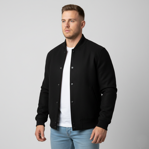 Man wearing a black varsity jacket over a white shirt and light blue jeans on a gray background