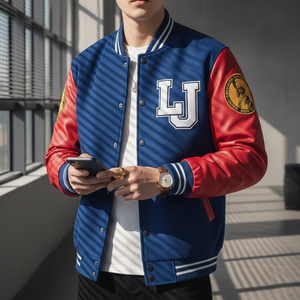 A boy wearing blue and red letterman jacket, stand next to window, holding phone.