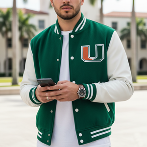 Person wearing a green and white varsity jacket with a logo, holding a phone outdoors.