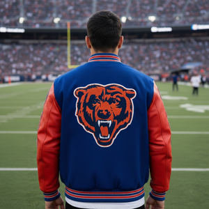 Person wearing a blue and red letterman jacket with a bear logo on a football field.
