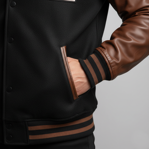 Black varsity jacket with brown leather sleeves and trim on a gray background