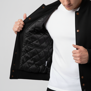 Person wearing a black quilted jacket with a white shirt underneath on a light gray background