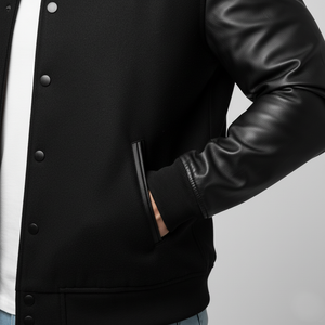 Black varsity jacket with leather sleeves on a gray background