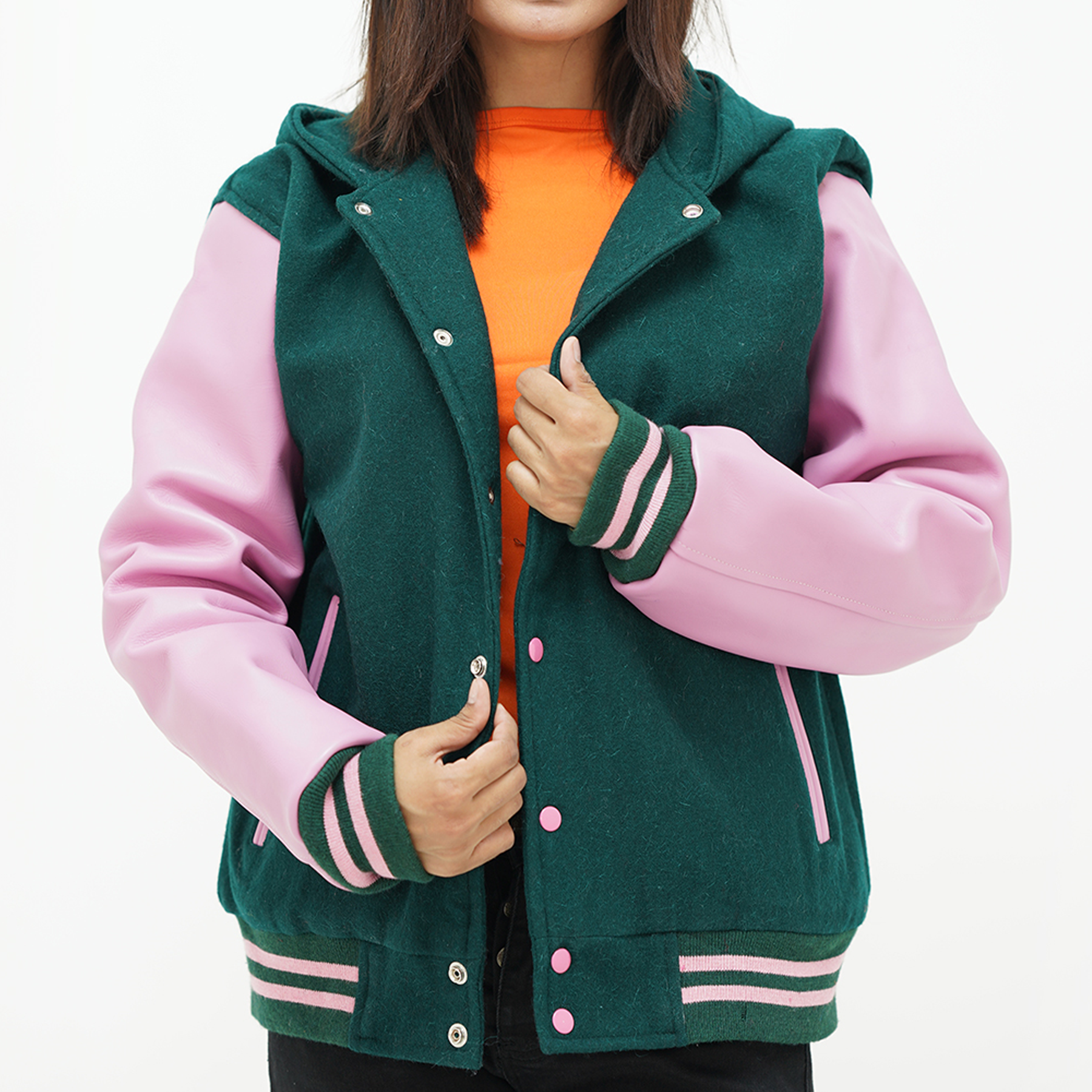A woman wearing a hooded jacket with a dark green wool body and pink leather sleeves, featuring a ribbed collar, pink stripes, and two leather-edged side pockets.