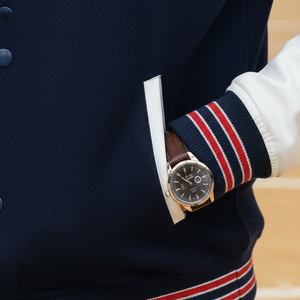 Person wearing a navy jacket with a white shirt and striped sleeves, holding a watch.