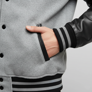 Person wearing a gray varsity jacket with black and gray striped sleeves, holding a phone.
