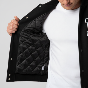 Person wearing a black quilted jacket with a white shirt underneath on a light gray background