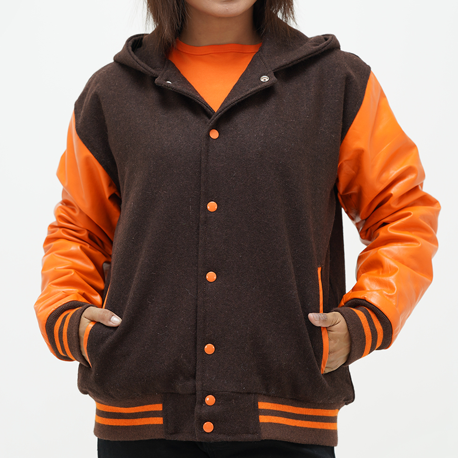 A woman wearing a chocolate brown varsity jacket with old gold leather sleeves, featuring a hood, ribbed cuffs, and a front with coated snap-button fastening.