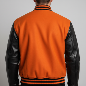 Orange varsity jacket with black leather sleeves on a gray background
