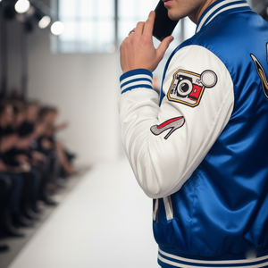 Person wearing a blue and white jacket with patches on a blurred fashion show background