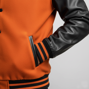 Orange varsity jacket with black leather sleeves on a gray background