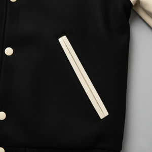 Black jacket with beige buttons and trim on a light gray background