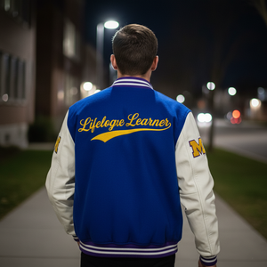 Person wearing a blue and white letterman jacket with 'Lifelong Learner' on the back at night.