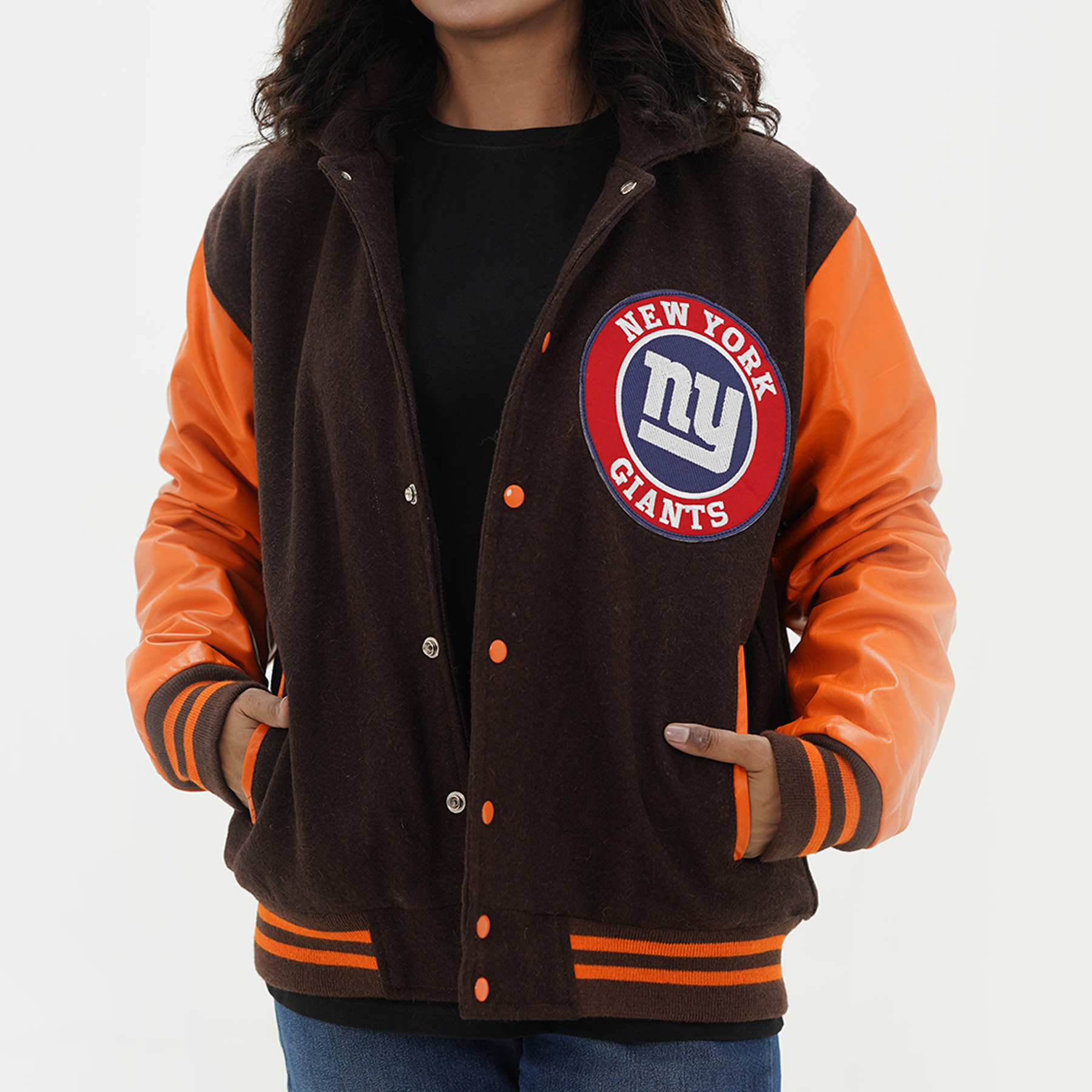 A woman wearing a brown and gold New York Giants varsity hoodie jacket with faux leather arms, featuring the team's logo on the front.