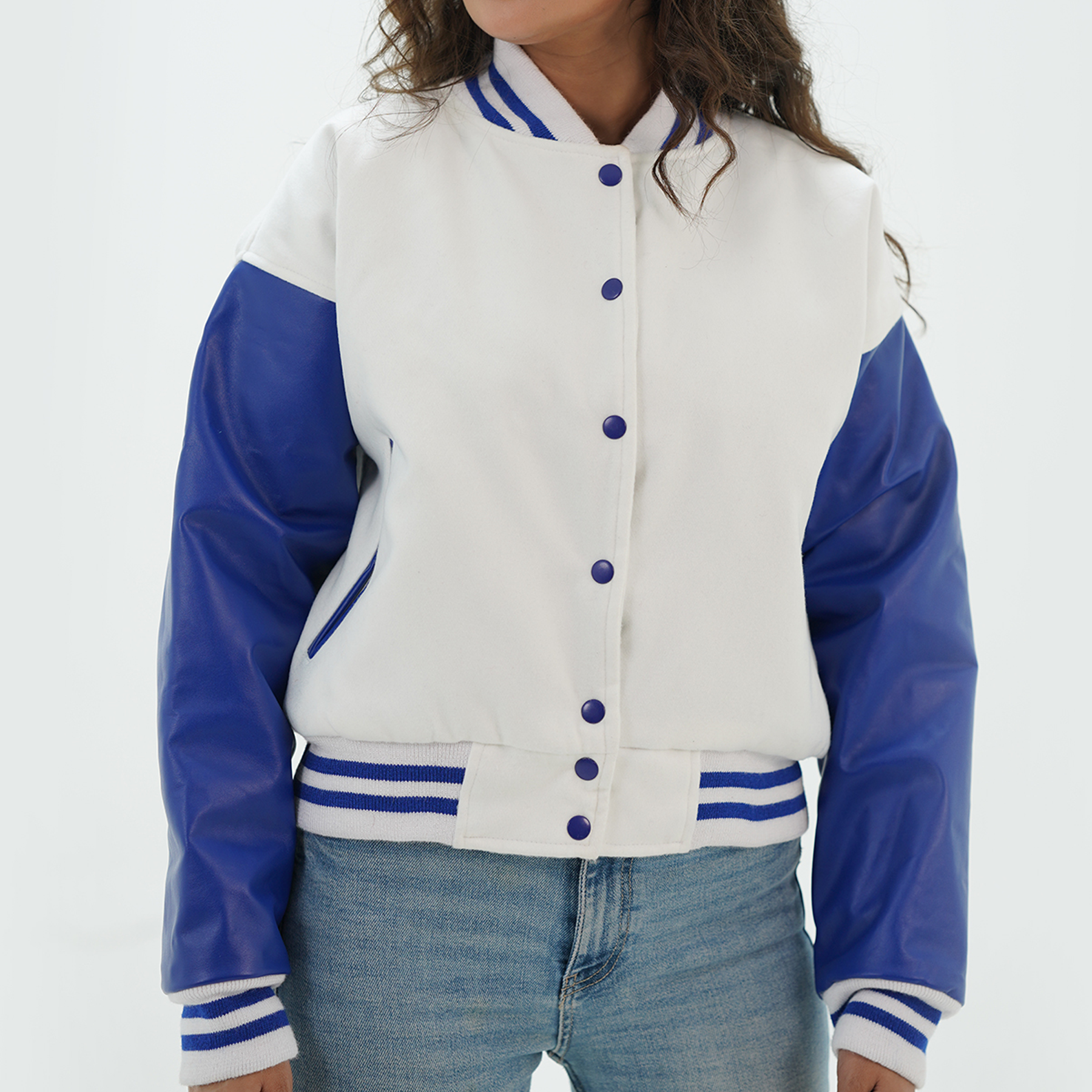 A woman wearing a white and blue leather and wool varsity jacket with a standing collar, featuring two side pockets and a front with snap buttons.