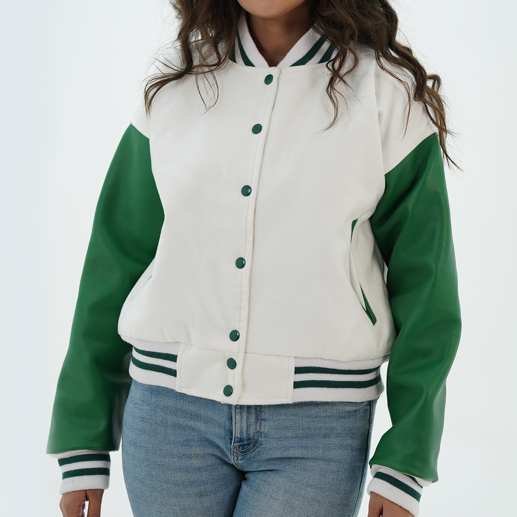 A woman wearing a white and green leather varsity jacket with a standing collar, featuring two side pockets and a front with coated snap-button fastening.
