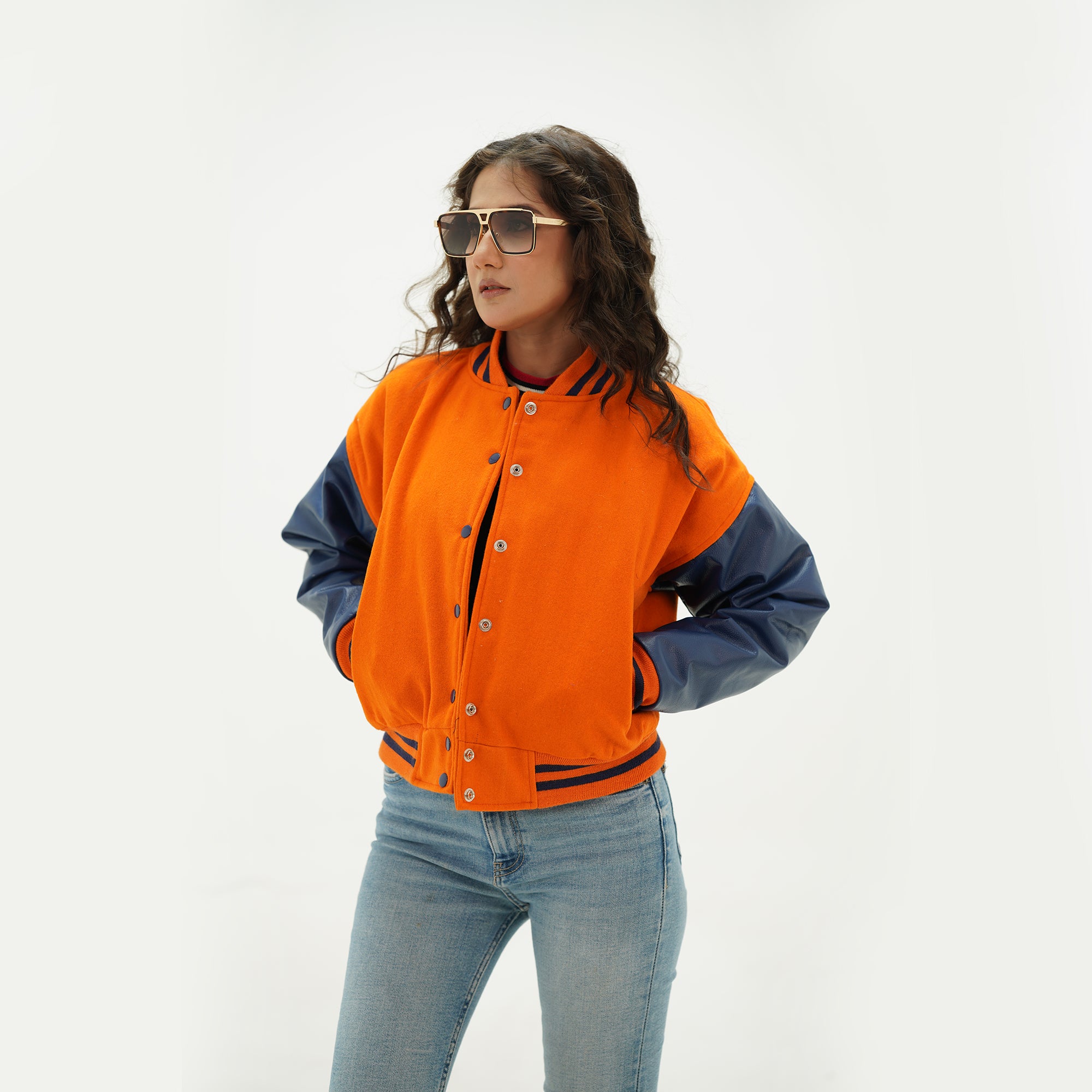 Three-quarter view of women's cropped varsity jacket highlighting orange body, java plum sleeves, snap button closure, and cropped length design