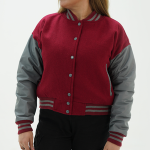 A woman wearing a magenta and gray letterman jacket with leather arms and a wool body, featuring a classic ribbed collar, ribbed cuffs, and side pockets.