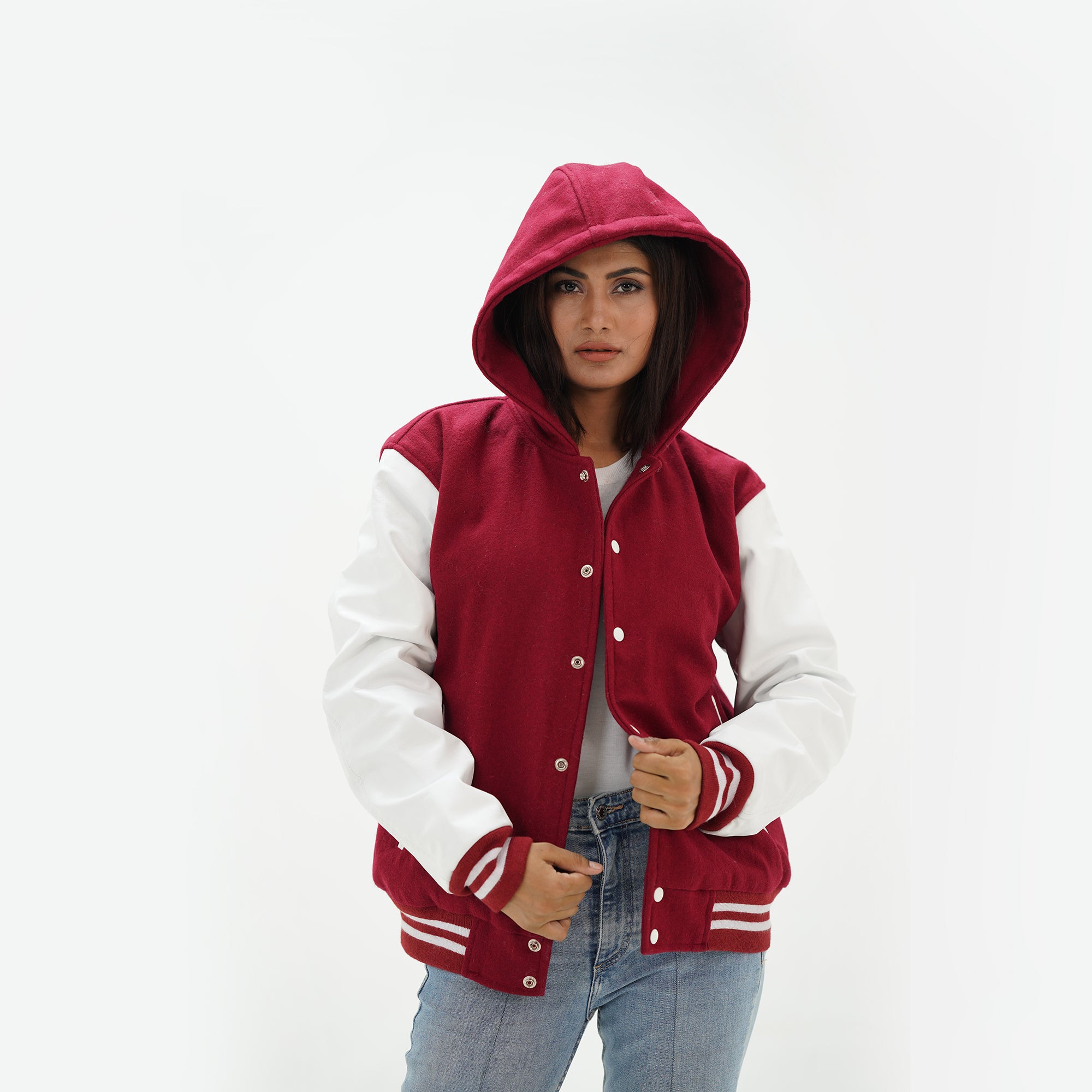 Three-quarter view of women's magenta hooded varsity jacket highlighting snap buttons, hood detail, side pockets, and magenta-white color scheme