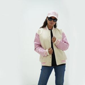 Three-quarter angle of women's off white and pink letterman jacket highlighting snap buttons, side pockets, and soft color palette