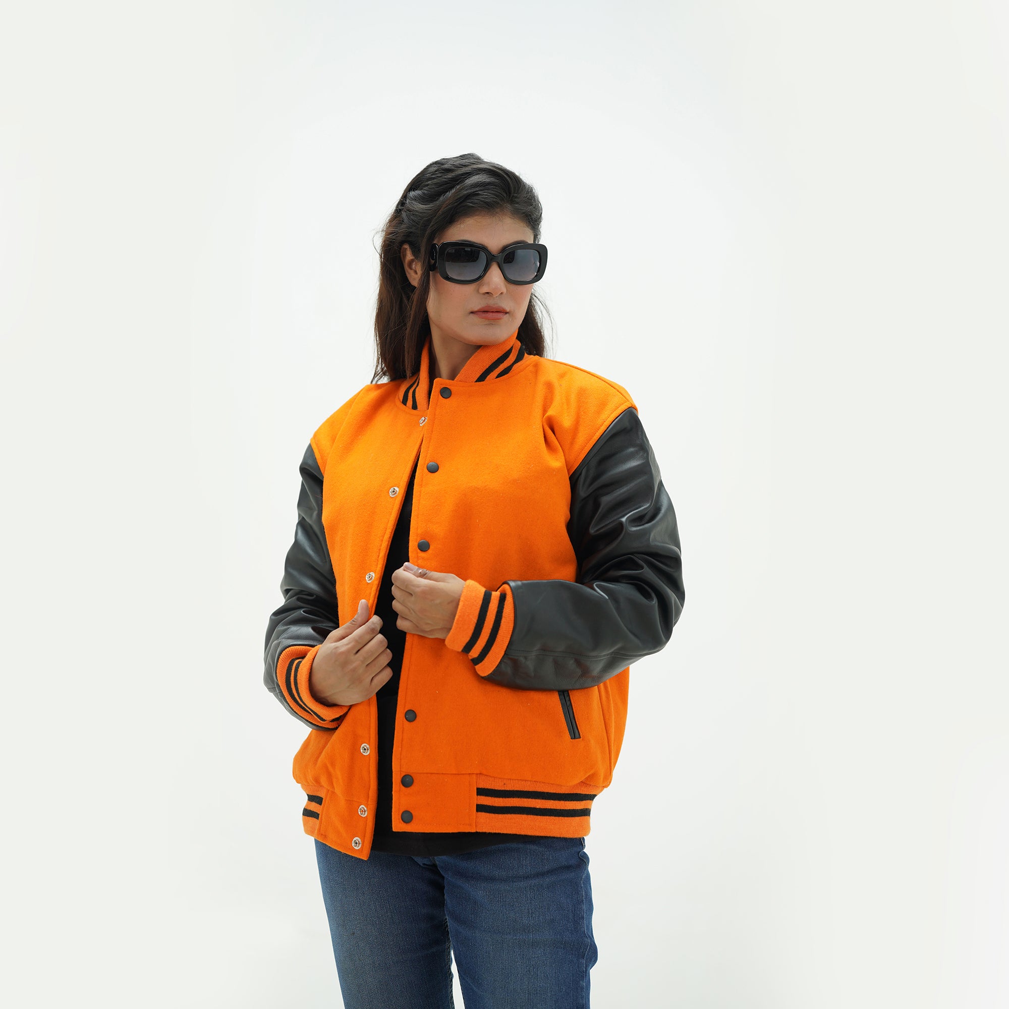 Side profile of women's orange varsity jacket with black leather sleeves showing ribbed cuffs and tailored feminine fit