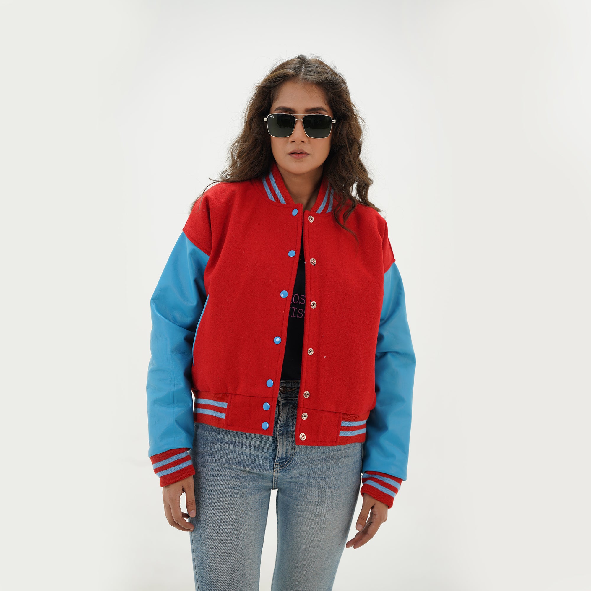 Three-quarter view of women's red and sky blue varsity jacket highlighting snap buttons, side pockets, and vibrant red-sky blue color combination